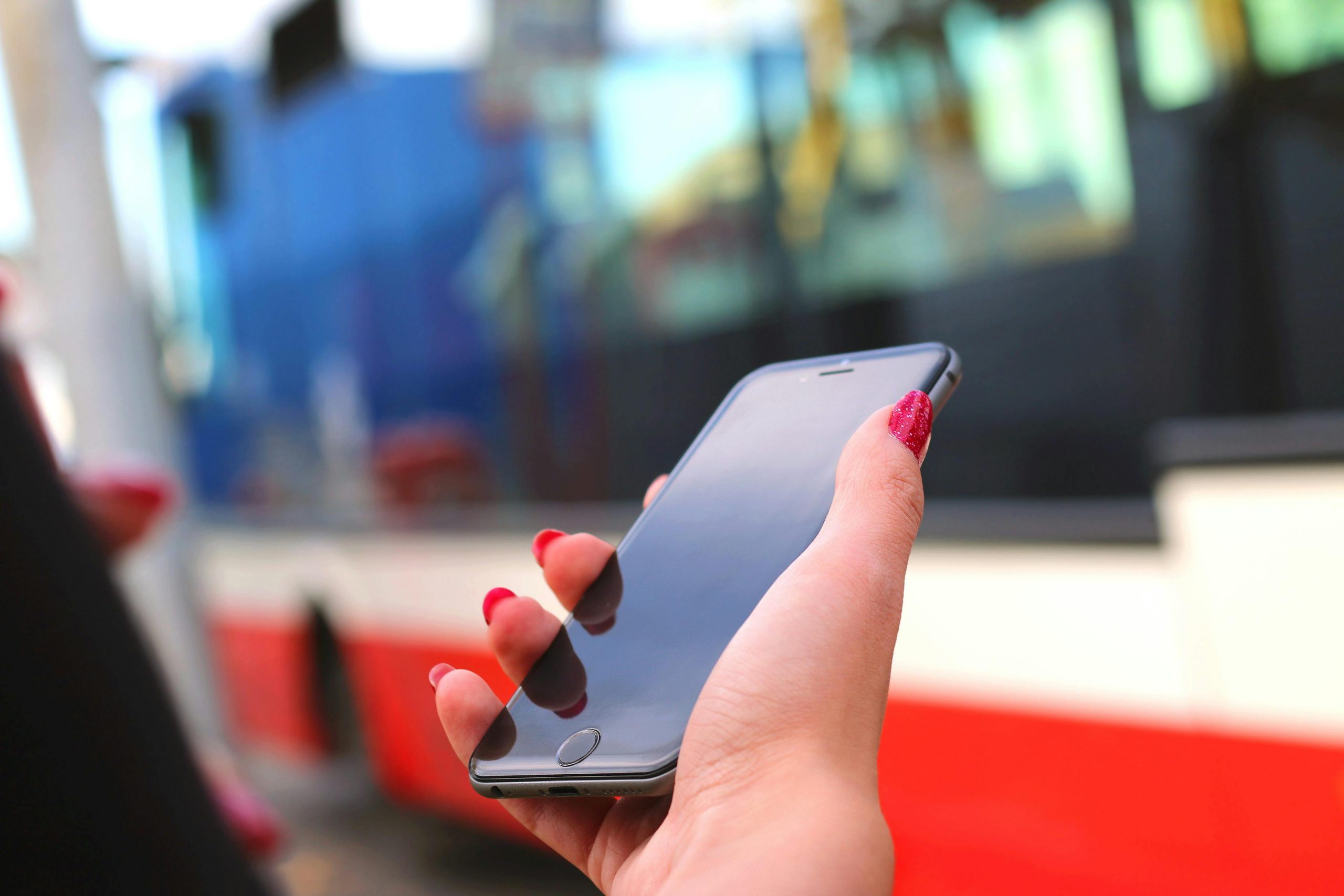 Close-up of a woman's hand holding a smartphone at a bus station, showcasing public transportation wait.